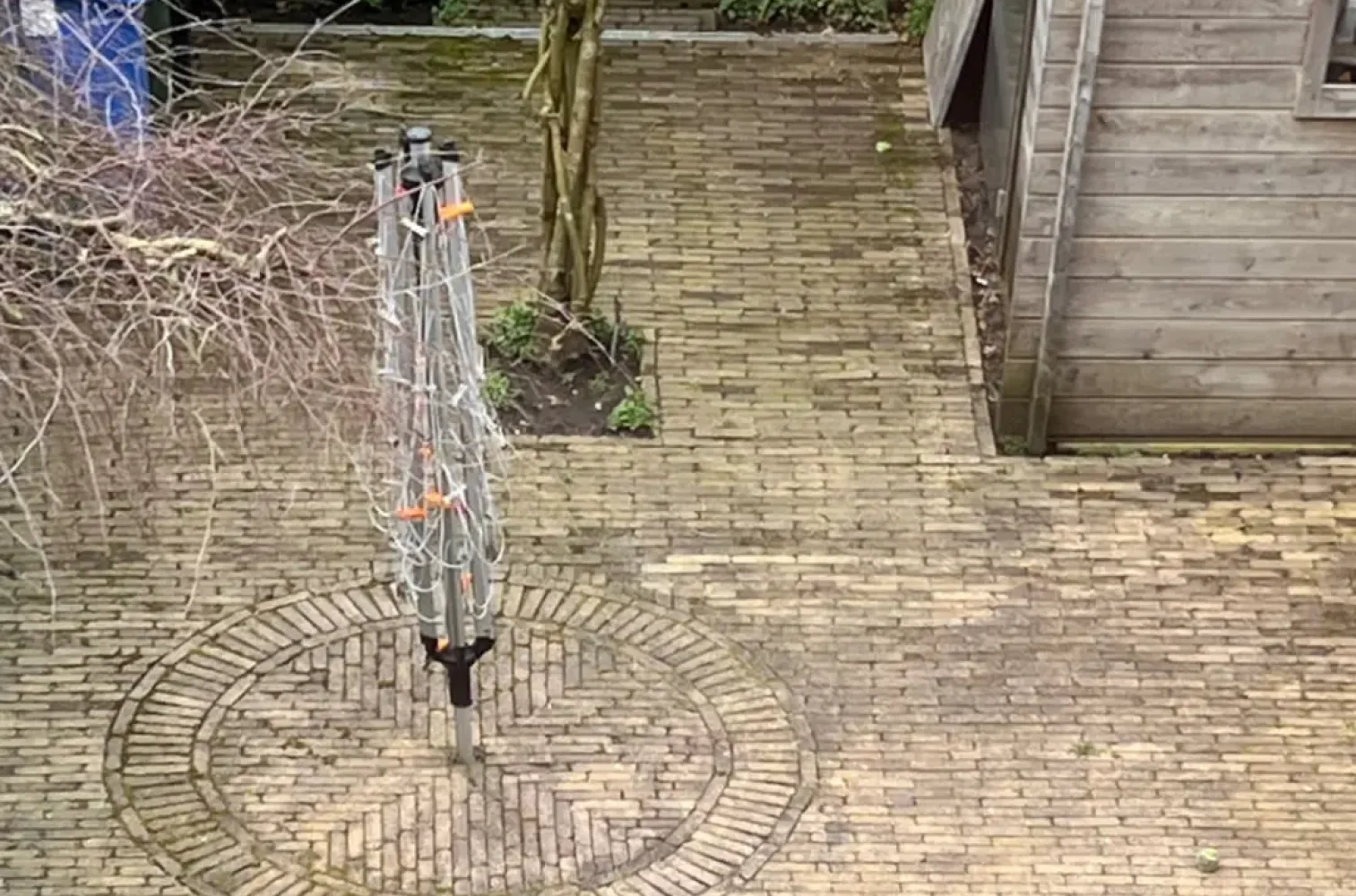 Before foto van de sfeervolle tuin in Hillegersberg, voordat Keko Hoveniers aan de slag ging met de nieuwe aanleg. Op de foto zie je de rommelige oude betegeling, een wasmolen en de stam van de blauwe regen die ook in de nieuwe tuin staat. Ontdek meer tuinprojecten van Keko Hoveniers in Nootdorp, Wassenaar, Pijnacker, Rijswijk, Berkel en Rodenrijs.