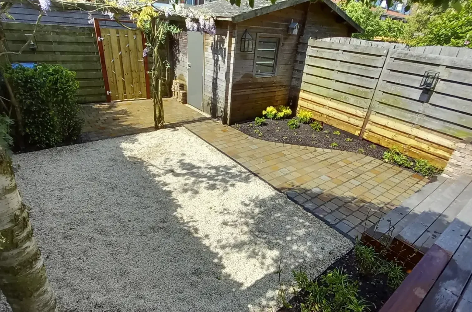 Sfeervolle tuin in Hillegersberg, ontworpen en aangelegd door Keko Hoveniers. De tuin begint vanuit de linkerhoek van het huis met een houten vlonder, die met twee treden naar de tuin leidt. Aan de rechterzijde liggen tegels in een halve golfvorm, omringd door kleine struiken. Aan de linkerkant is grind geplaatst voor de wasmolen. Langs de houten vlonder zijn borders gecreëerd met bloemen en struiken. Aan het einde van de tuin is een betegeld gedeelte met een hoge struik die de afvalbak verbergt. De schuur is niet aangepast maar past goed bij de rest van de tuin. In het midden van de tuin staat de oorspronkelijke boom: de blauwe regen op stam, net zoals voor Keko Hoveniers aan de tuin begon.